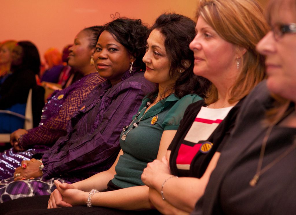 A row of ethnically diverse Queen’s Nurses in an audience