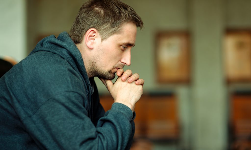 A troubled man holds his head in his hands in a green room