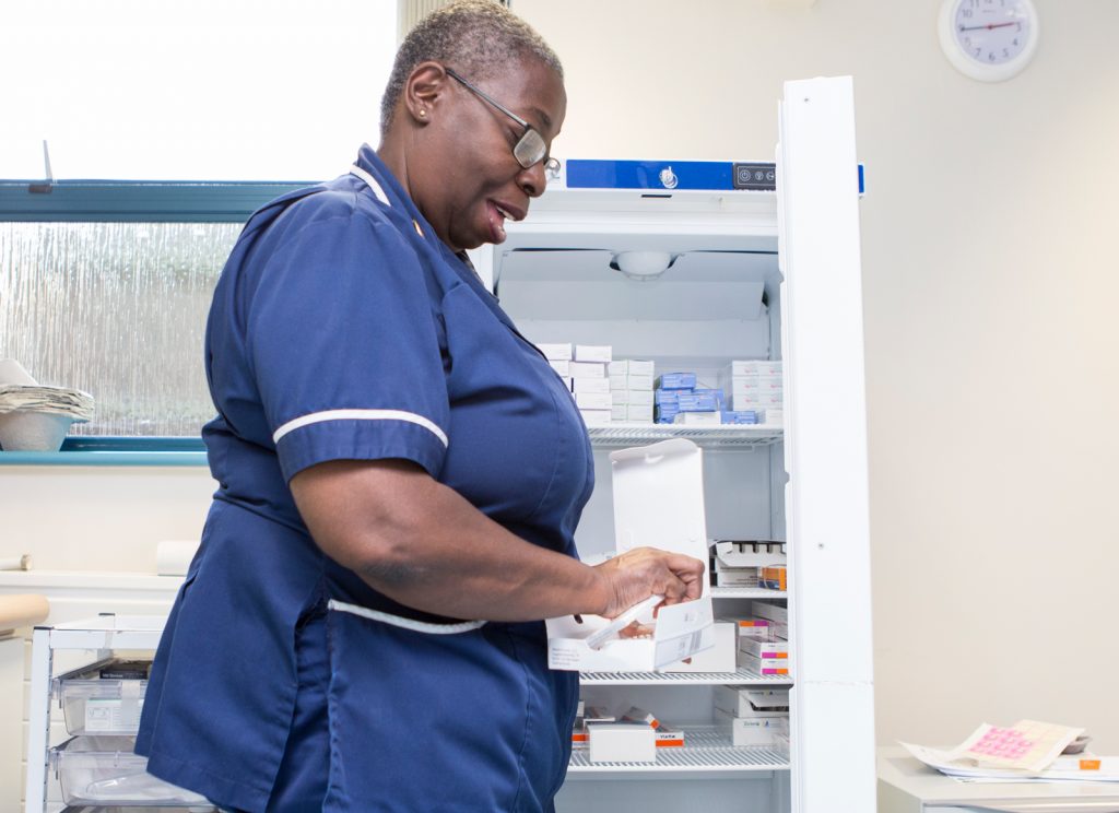 General Practice Nurse standing looking at drugs to prescribe