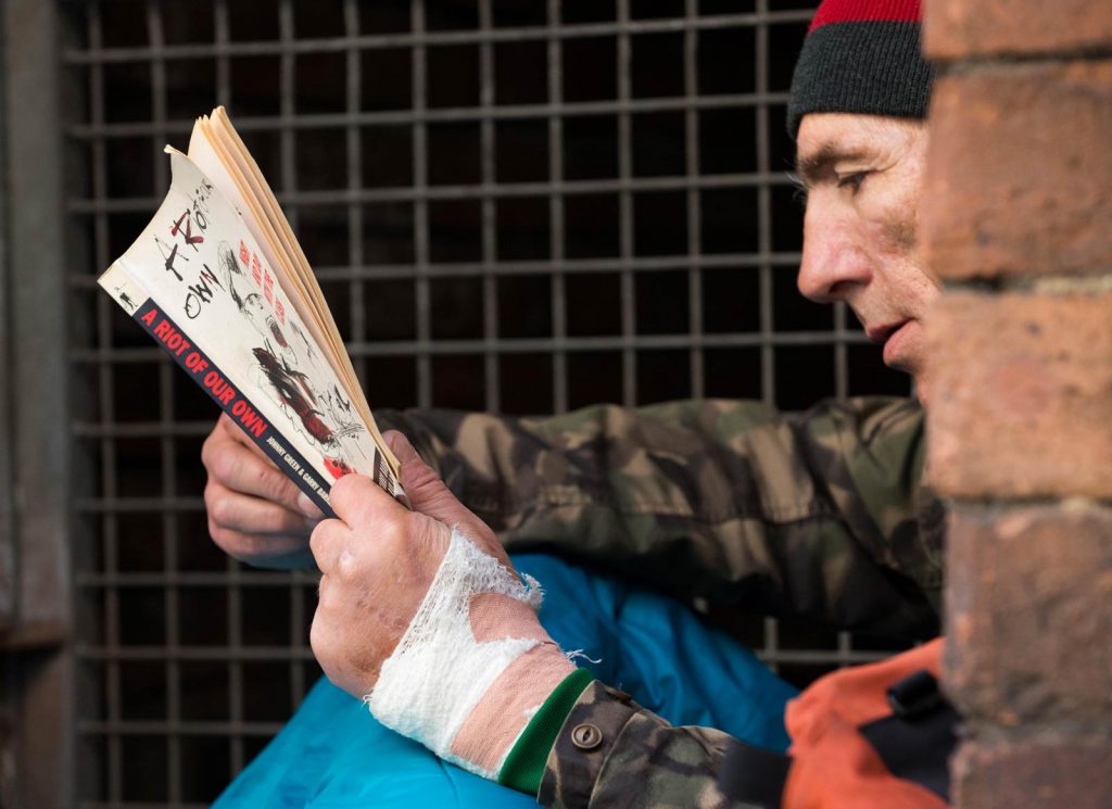 A homeless man reading a book while in his sleeping bag