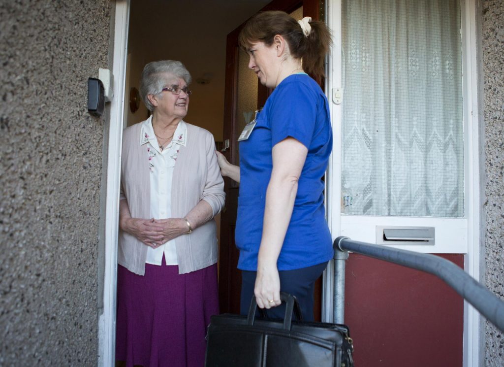 A district nurse in uniform at the front door of a patient