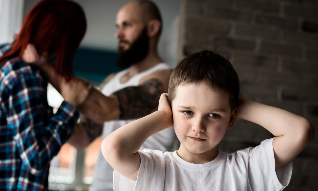 a young boy covers his ears while his parents argue