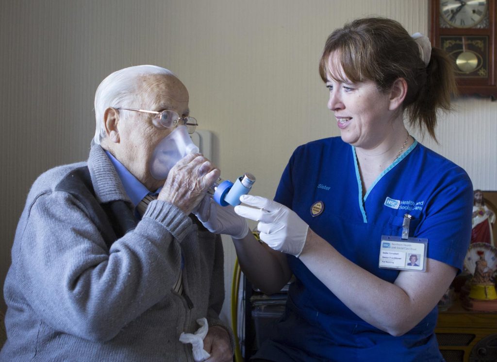 A district nurse helping an elderly man with an inhaler